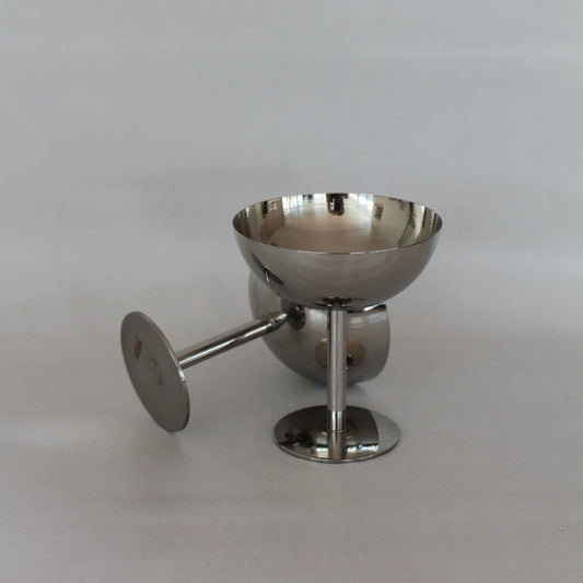 o stål cocktailglas eller champagne glas med en minimalistisk og moderne stil. Et glas står oprejst, mens det andet ligger på siden. Glasene har en glat, poleret overflade og en enkel stil, præsenteret mod en neutral baggrund.