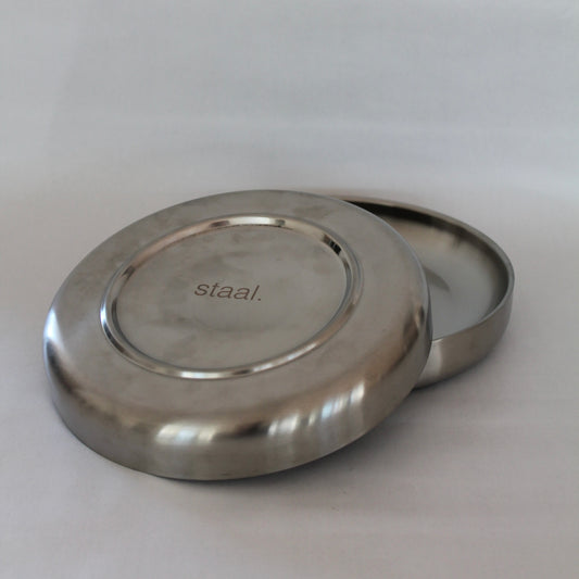 To stål tallerkener i minimalistisk design, hvor den ene tallerken ligger ovenpå den anden med bunden opad. Bunden viser et indgraveret logo med teksten 'staal.' på en neutral baggrund.